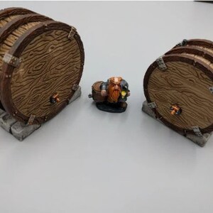 May include: Three wooden barrels with metal accents and a small figurine of a dwarf holding a barrel. The barrels are brown and have a wood grain texture. The dwarf is wearing a red and brown outfit and has a beard.