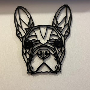 May include: Black geometric silhouette of a French bulldog head, a popular breed of dog, on a white wall.