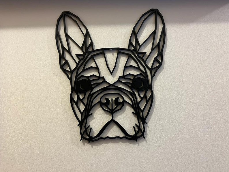 May include: Black geometric silhouette of a French bulldog head, a popular breed of dog, on a white wall.