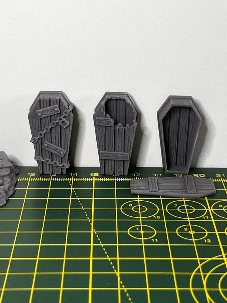 May include: Three gray plastic miniature coffins. One coffin is closed, one is open with a broken lid, and one has a chain and padlock on the lid.