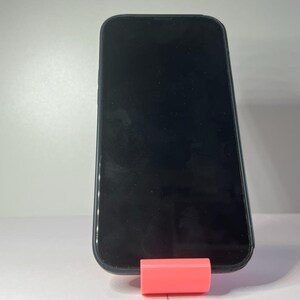 May include: A black smartphone with a blank screen is standing upright on a pink stand.