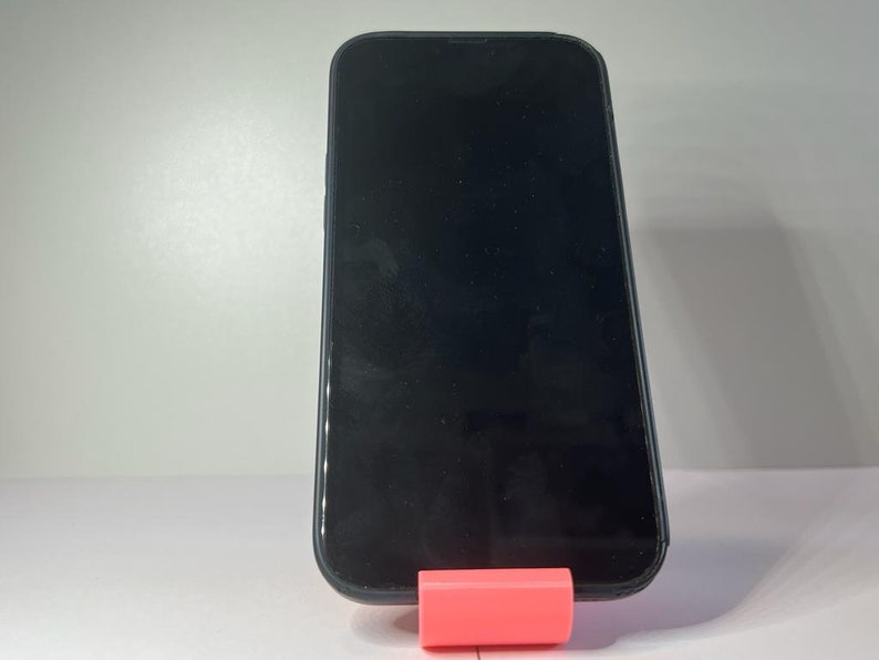 May include: A black smartphone with a blank screen is standing upright on a pink stand.