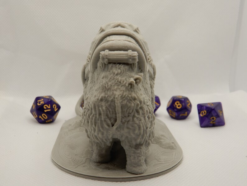 May include: A gray 3D printed miniature of a furry creature with a saddle and a rope attached to the back. The creature is standing on a round base. There are four purple dice with gold numbers in the background.