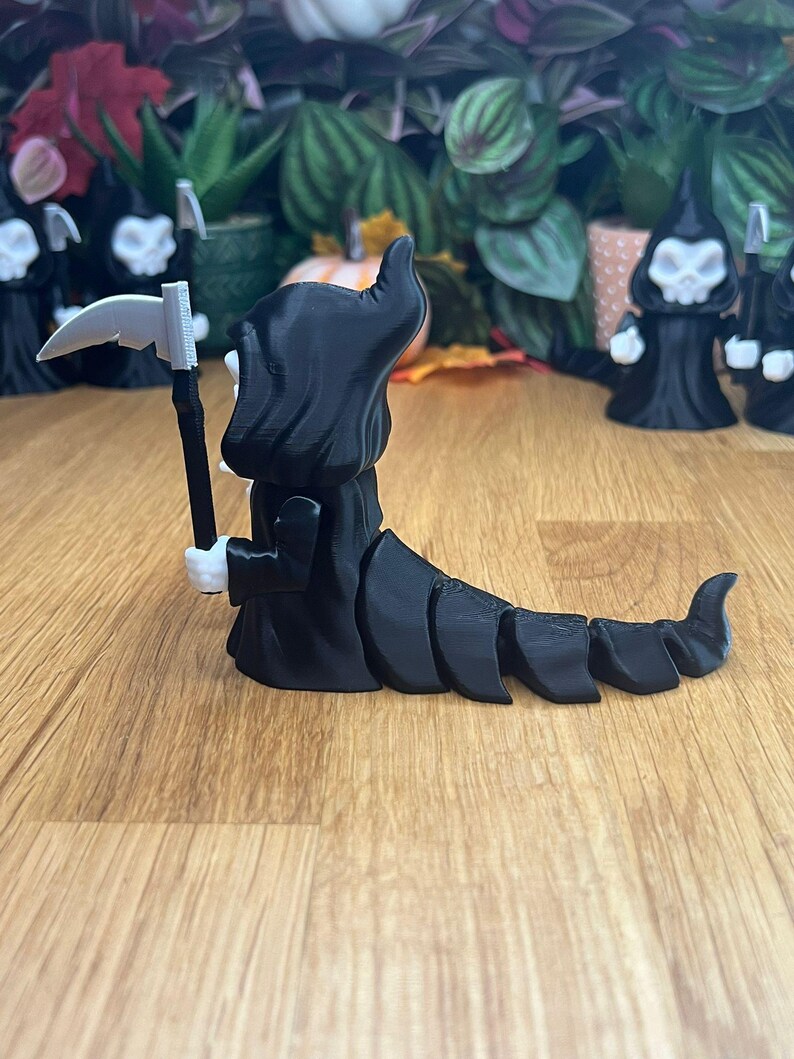 May include: Black skeletal figure with a scythe and a segmented tail. The figure is wearing a black hooded robe and has a white face.