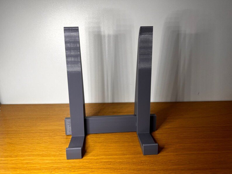 May include: A gray plastic stand with two vertical supports and a horizontal base. The stand is designed to hold a plate or other flat object.