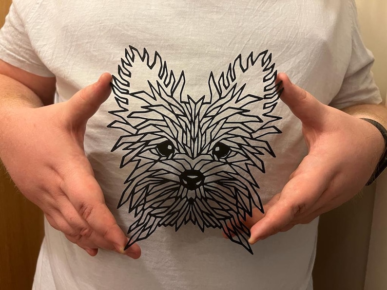 May include: A black and white geometric paper cut-out of a Yorkshire Terrier dog's face.