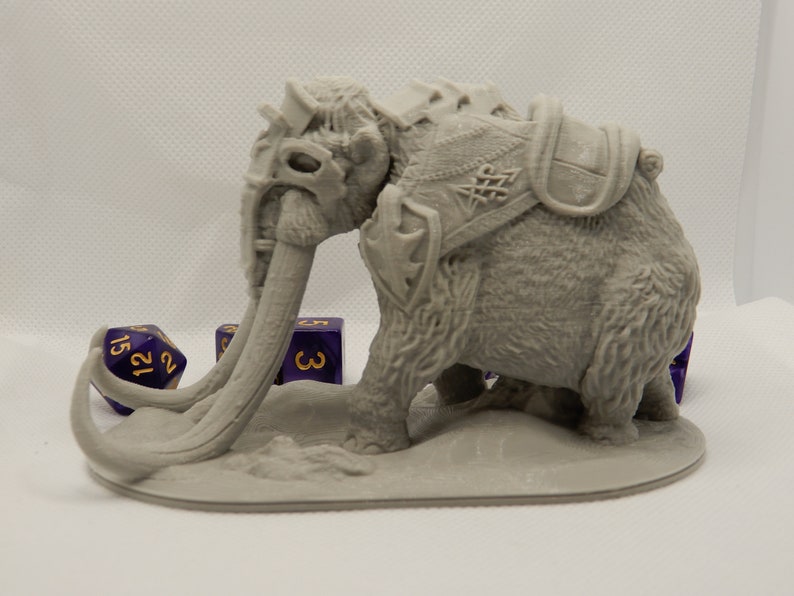 May include: A gray 3D printed miniature of a mammoth with a saddle and tusks. The mammoth is standing on a gray base. There are three purple dice with gold numbers on the base.