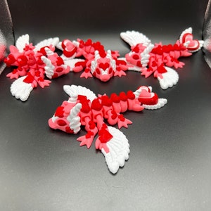 Puede incluir: Cinco peque&ntilde;as figuritas aladas de color rosa y blanco con corazones rojos. Las figuritas est&aacute;n hechas de un material suave y flexible y tienen un aspecto caprichoso y caricaturesco.