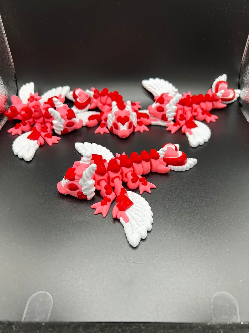 Puede incluir: Cinco peque&ntilde;as figuritas aladas de color rosa y blanco con corazones rojos. Las figuritas est&aacute;n hechas de un material suave y flexible y tienen un aspecto caprichoso y caricaturesco.