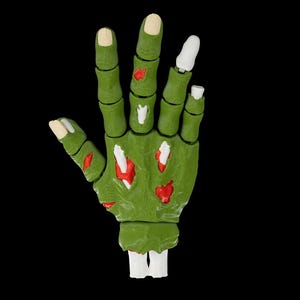 Peut inclure: Une main de zombie verte avec des éclaboussures de sang rouge et des os blancs. La main est ouverte et les doigts sont écartés.