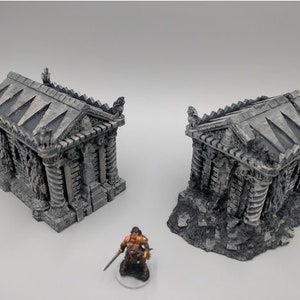 May include: Two gray stone miniature buildings with intricate details, resembling ancient tombs or temples. The buildings are set on a base of gray and brown textured material, suggesting a ruined or overgrown setting.