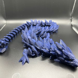 May include: A 3D printed blue dragon figurine with a spiky, crystalline texture. The dragon is posed with its head raised and its tail curled.