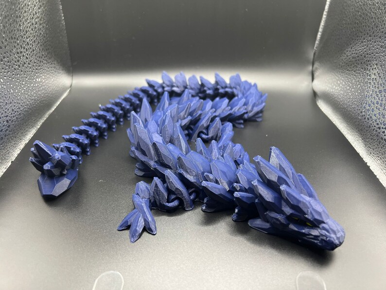 May include: A 3D printed blue dragon figurine with a spiky, crystalline texture. The dragon is posed with its head raised and its tail curled.