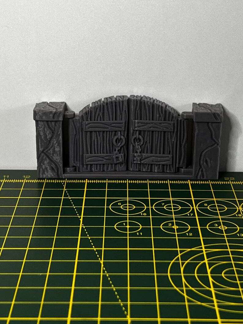 May include: A gray, wooden gate with a chain and padlock. The gate is closed and has a slightly arched top. The gate is sitting on a green cutting mat.