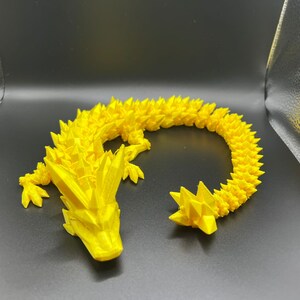May include: A yellow 3D printed dragon figurine with a spiky, textured design. The dragon is curled into a circle with its tail touching its head.