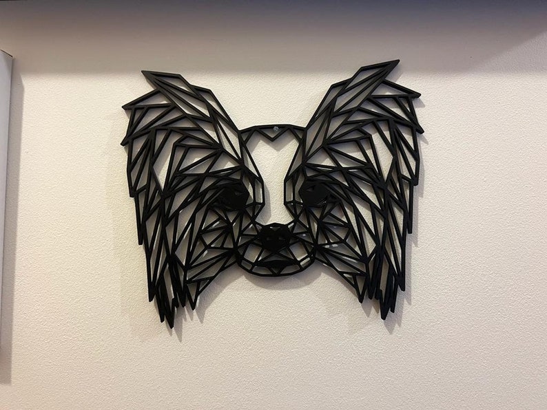 Puede incluir: Arte de pared geom&eacute;trico negro que representa la cabeza de un perro con orejas grandes. El arte est&aacute; hecho de metal negro delgado y est&aacute; montado en una pared blanca.