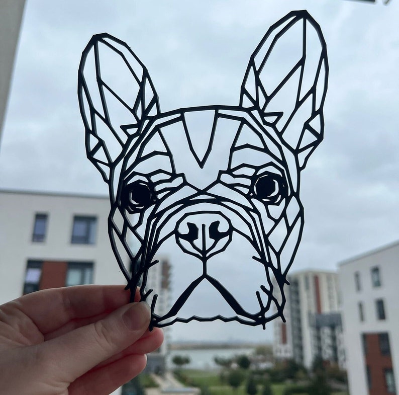 May include: Black paper cut-out of a French Bulldog's head. The design is geometric and abstract.