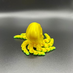 May include: A yellow 3D printed octopus with green accents. The octopus has eight tentacles and a round head.