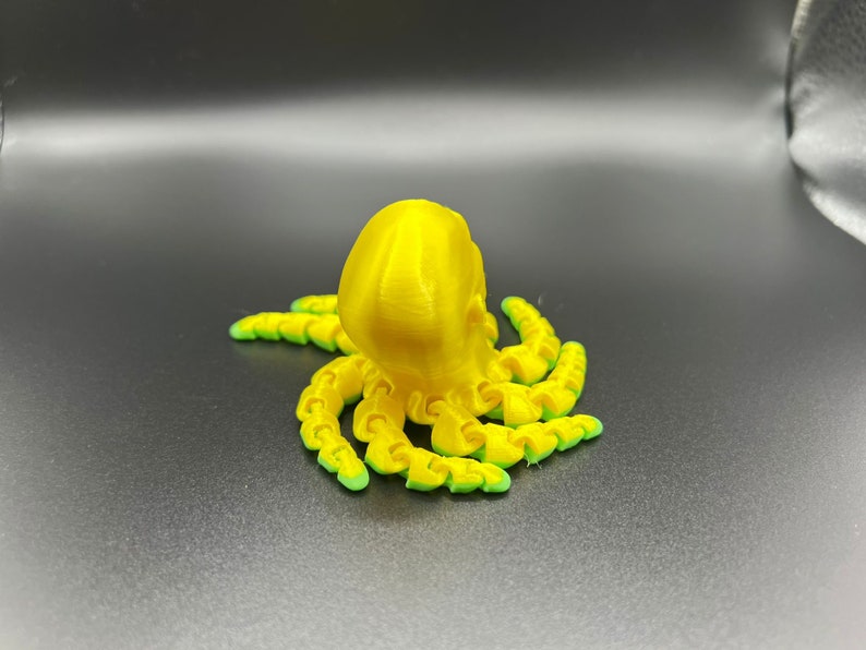 May include: A yellow 3D printed octopus with green accents. The octopus has eight tentacles and a round head.