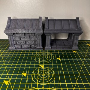 May include: Two grey 3D printed miniature stone structures with arched openings. The structure on the left has a solid wall, while the structure on the right has an open interior. Both structures have a flat roof.