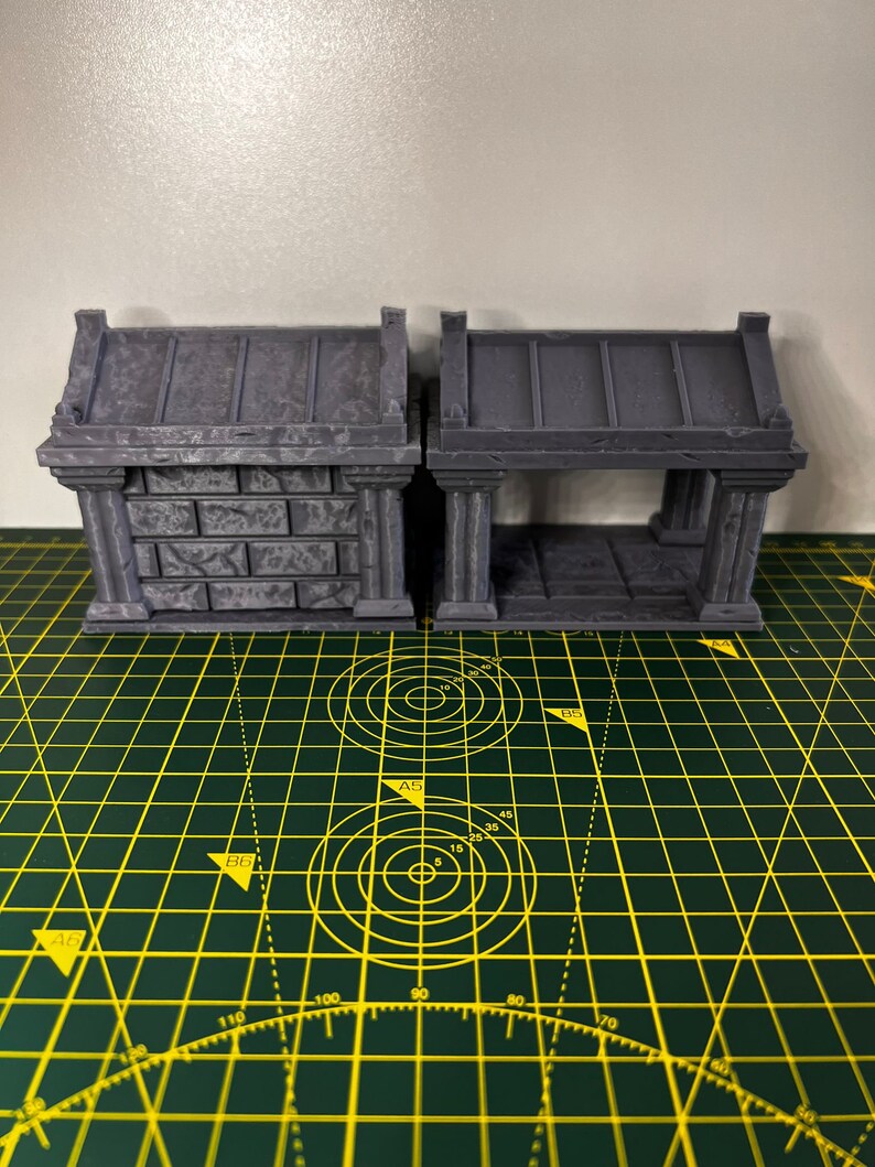 May include: Two grey 3D printed miniature stone structures with arched openings. The structure on the left has a solid wall, while the structure on the right has an open interior. Both structures have a flat roof.