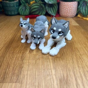 Peut inclure: Trois figurines de loup grises et blanches avec des membres articul&eacute;s. Les loups sont en position assise et couch&eacute;e.