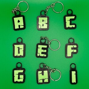 May include: Nine black keychains with green letters spelling out the word "ABCDEFGHI". Each keychain has a silver ring.