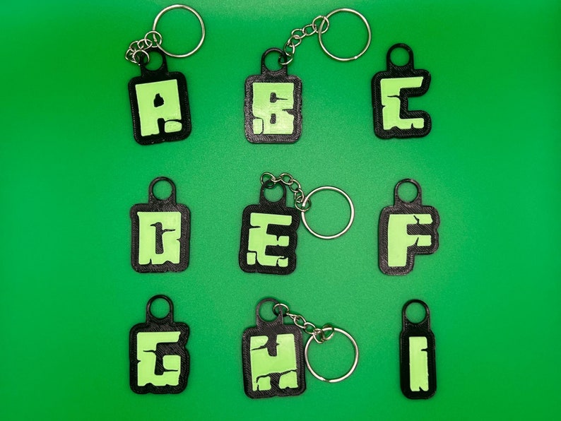 May include: Nine black keychains with green letters spelling out the word "ABCDEFGHI". Each keychain has a silver ring.
