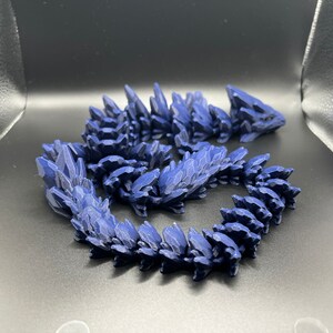 May include: A dark blue, 3D printed dragon figurine with a spiky, scaly design. The dragon is curled up in a coil shape.