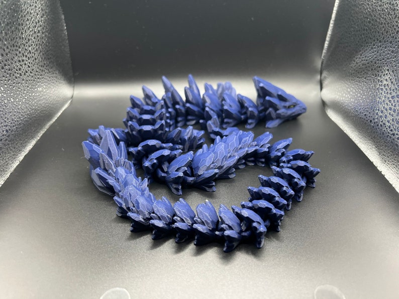May include: A dark blue, 3D printed dragon figurine with a spiky, scaly design. The dragon is curled up in a coil shape.