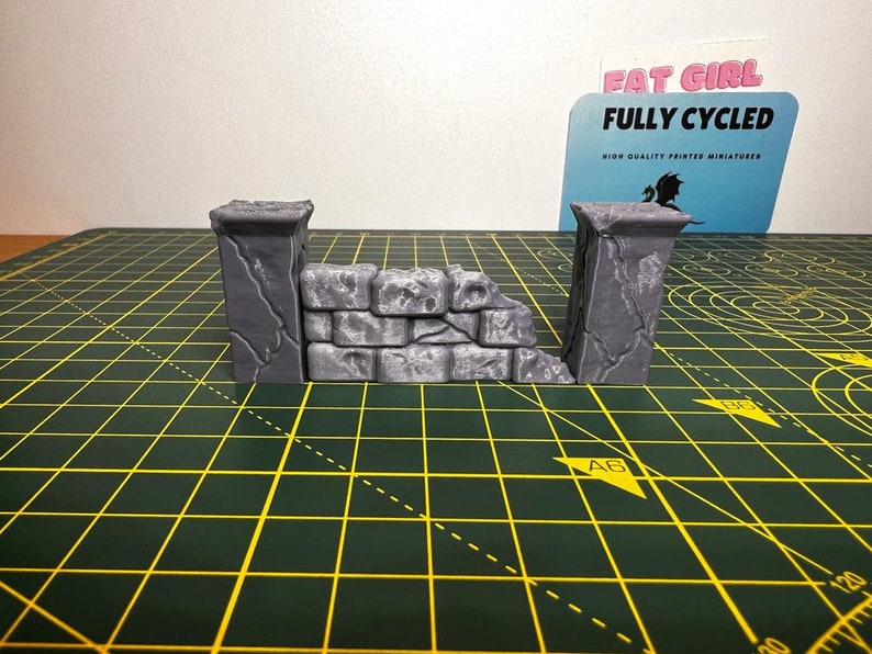 May include: A gray stone wall miniature with a broken section, perfect for tabletop gaming or miniature painting. The wall is made of two pillars and a connecting section with a rough, textured surface.
