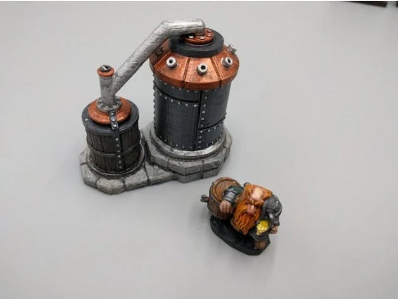 May include: A miniature model of a steampunk-style distillery with a copper and metal tank, a pipe, and a barrel. A small, painted figurine of a dwarf with a beard and a barrel sits in front of the distillery.