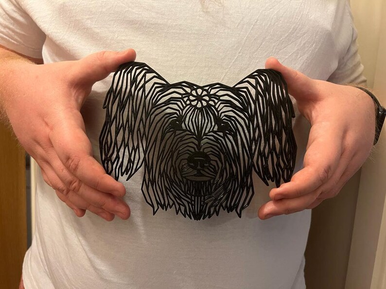 Op de afbeelding: Een zwart papieren uitsnijding van een hondenkop, met een gedetailleerd ontwerp van vacht en gezichtskenmerken.