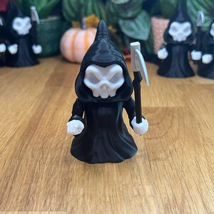 May include: A black 3D printed figurine of the Grim Reaper holding a scythe. The figurine is wearing a black hooded robe and has a white skull face.