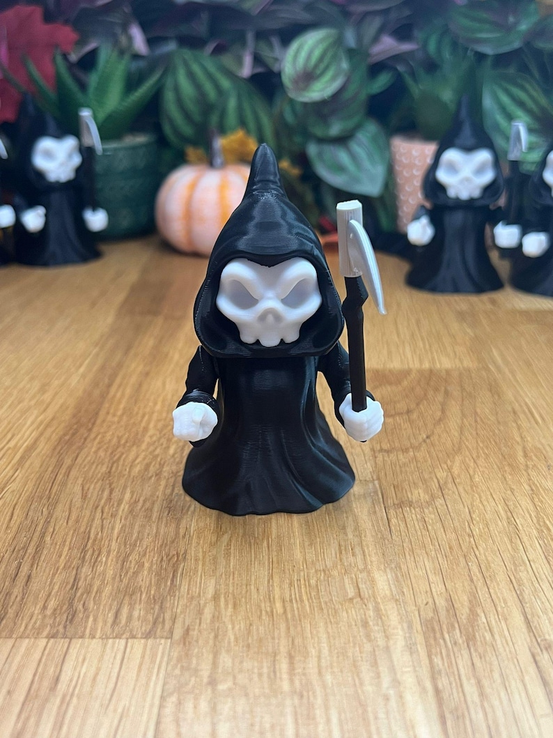 May include: A black 3D printed figurine of the Grim Reaper holding a scythe. The figurine is wearing a black hooded robe and has a white skull face.