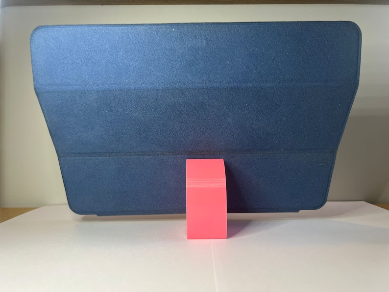 May include: A dark blue tablet case with a pink stand. The case is folded to create a stand for the tablet.
