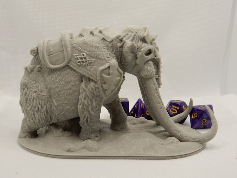 May include: A gray, 3D printed miniature of a mammoth with a saddle and armor. The mammoth has a long trunk and tusks. The miniature is posed standing on a base with four purple dice.