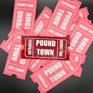 Puede incluir: Un mont&oacute;n de boletos de papel rosa con las palabras "Pound Town" y "Entrance" impresas en ellos. Un boleto es rojo y dice "Pound Town" y "Entrance" en blanco.