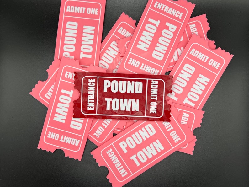 Puede incluir: Un mont&oacute;n de boletos de papel rosa con las palabras "Pound Town" y "Entrance" impresas en ellos. Un boleto es rojo y dice "Pound Town" y "Entrance" en blanco.