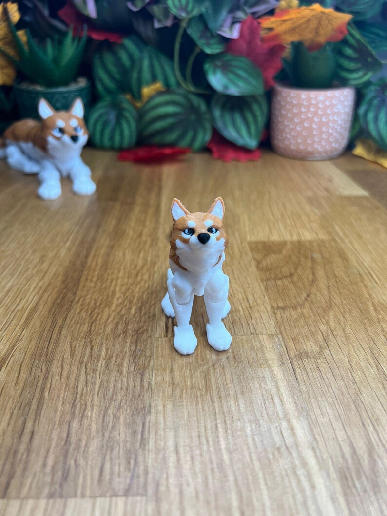 Peut inclure: Une petite figurine de chien en blanc et brun, assise sur une surface en bois. Le chien a un corps blanc avec des oreilles brunes, une queue brune et des marques brunes sur le visage.