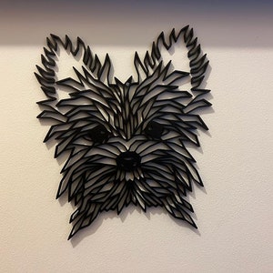 May include: Black and white geometric silhouette of a Yorkshire Terrier dog's head, made of layered paper or wood, mounted on a white wall.