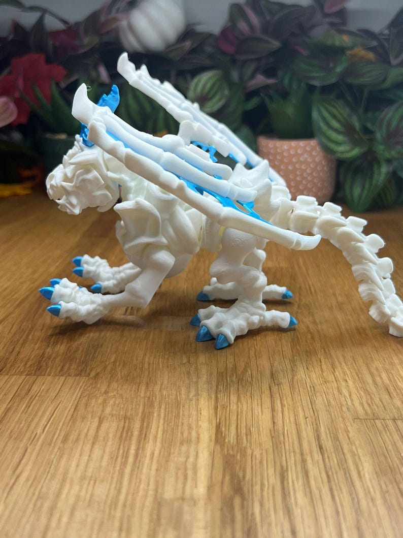 Puede incluir: Un esqueleto de drag&oacute;n de pl&aacute;stico blanco con detalles azules. El drag&oacute;n est&aacute; en posici&oacute;n sentada con las alas extendidas.