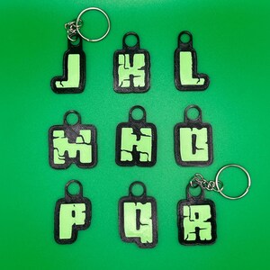 May include: Ten black keychains with green letters spelling out "J H L P U R" on a green background.