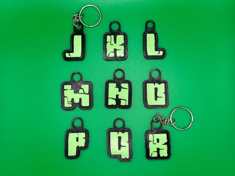 May include: Ten black keychains with green letters spelling out "J H L P U R" on a green background.