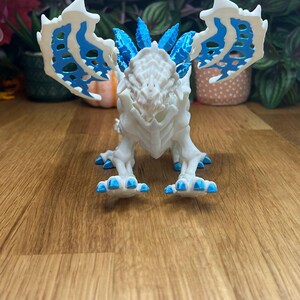 Puede incluir: Figura de drag&oacute;n esquel&eacute;tico blanco con detalles azules. El drag&oacute;n tiene una cresta puntiaguda y alas grandes.