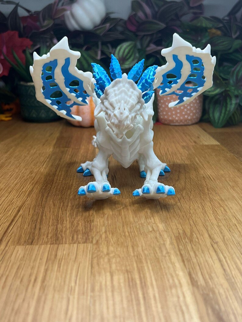 Puede incluir: Figura de drag&oacute;n esquel&eacute;tico blanco con detalles azules. El drag&oacute;n tiene una cresta puntiaguda y alas grandes.