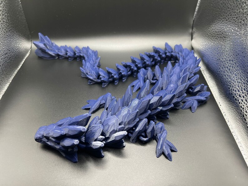 May include: A 3D printed blue dragon figurine with a spiky, crystalline texture. The dragon is curled up in a resting pose.