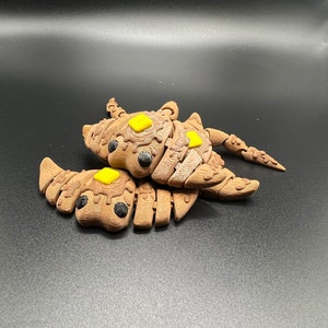 May include: Two brown, segmented, 3D printed creatures with yellow accents. The creatures are joined together and have a segmented, scorpion-like tail.