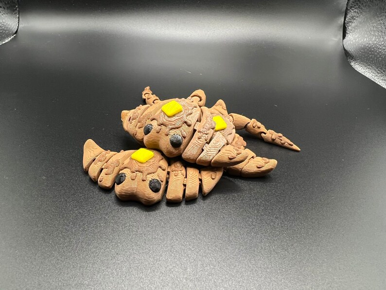 May include: Two brown, segmented, 3D printed creatures with yellow accents. The creatures are joined together and have a segmented, scorpion-like tail.