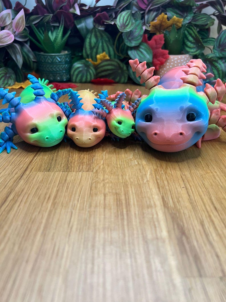 May include: Four colorful, 3D printed, rainbow axolotl figurines. The axolotls are arranged in a row, with the largest axolotl in the back and the smallest axolotl in the front. The axolotls are all facing the camera.
